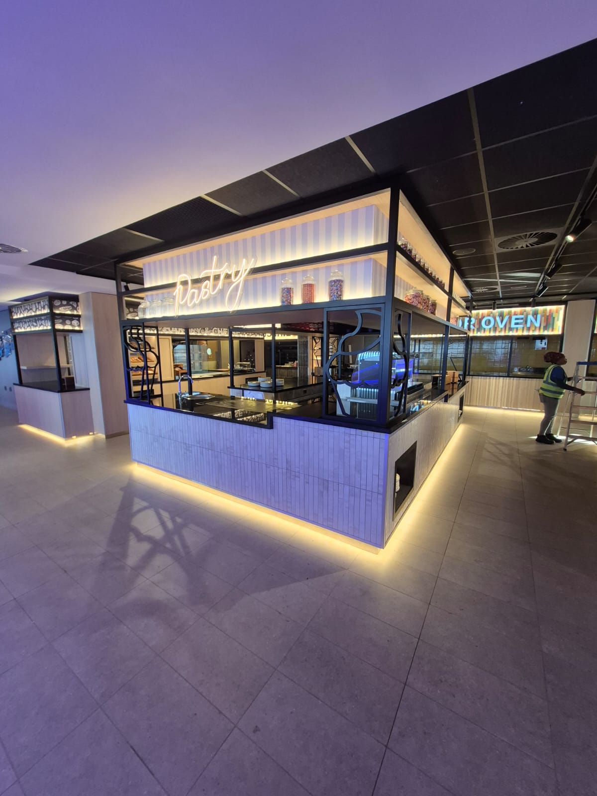 The Pastry station with neon signage, steel framing and a tiled counter lit from below