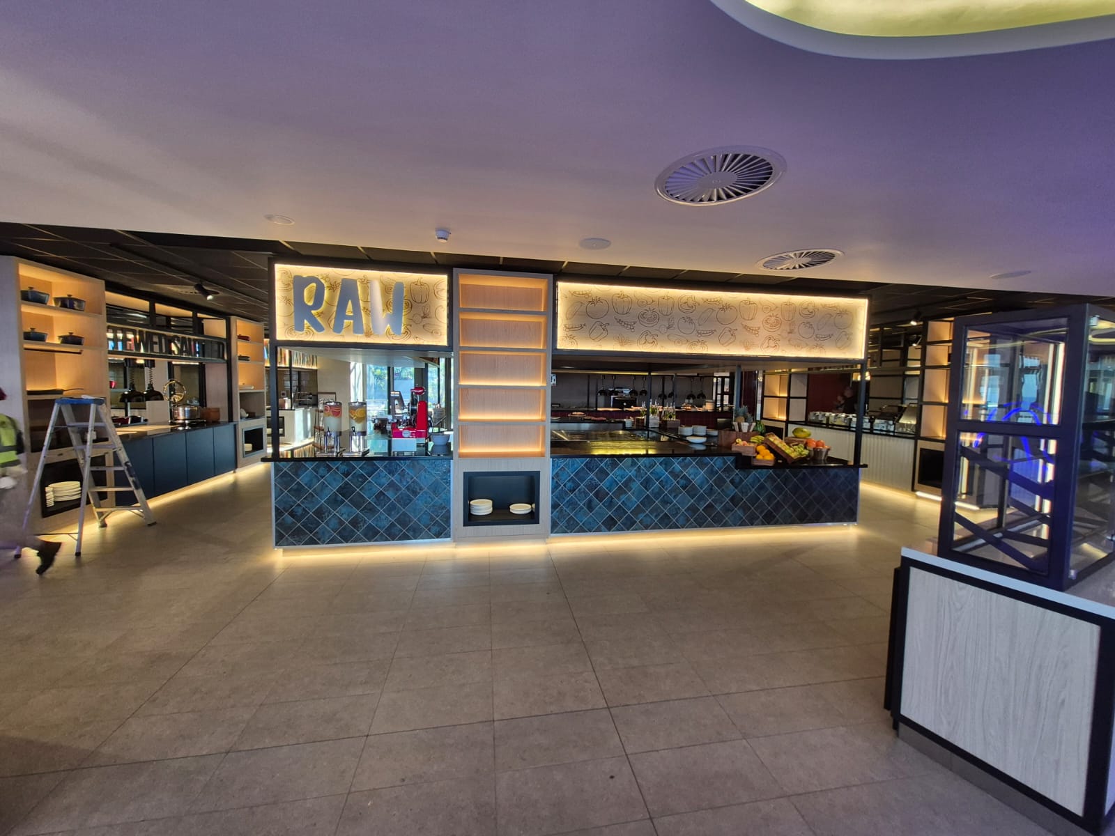The RAW salad station with a blue tiled counter front and backlit illustrated signage panel